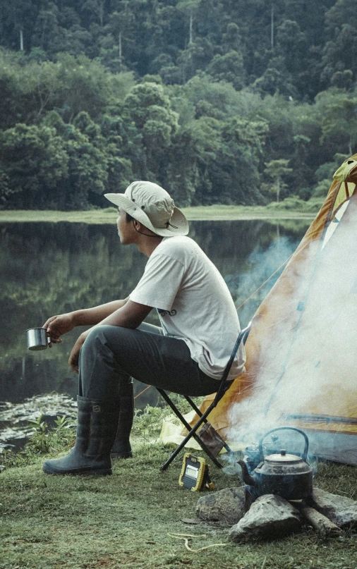 a man sitting on a chair outside next to a tent