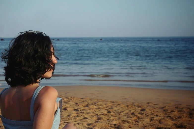 there is a woman sitting on the sand at the beach