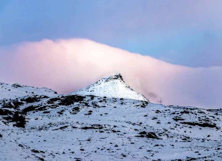 a very tall mountain covered in snow under a cloudy sky