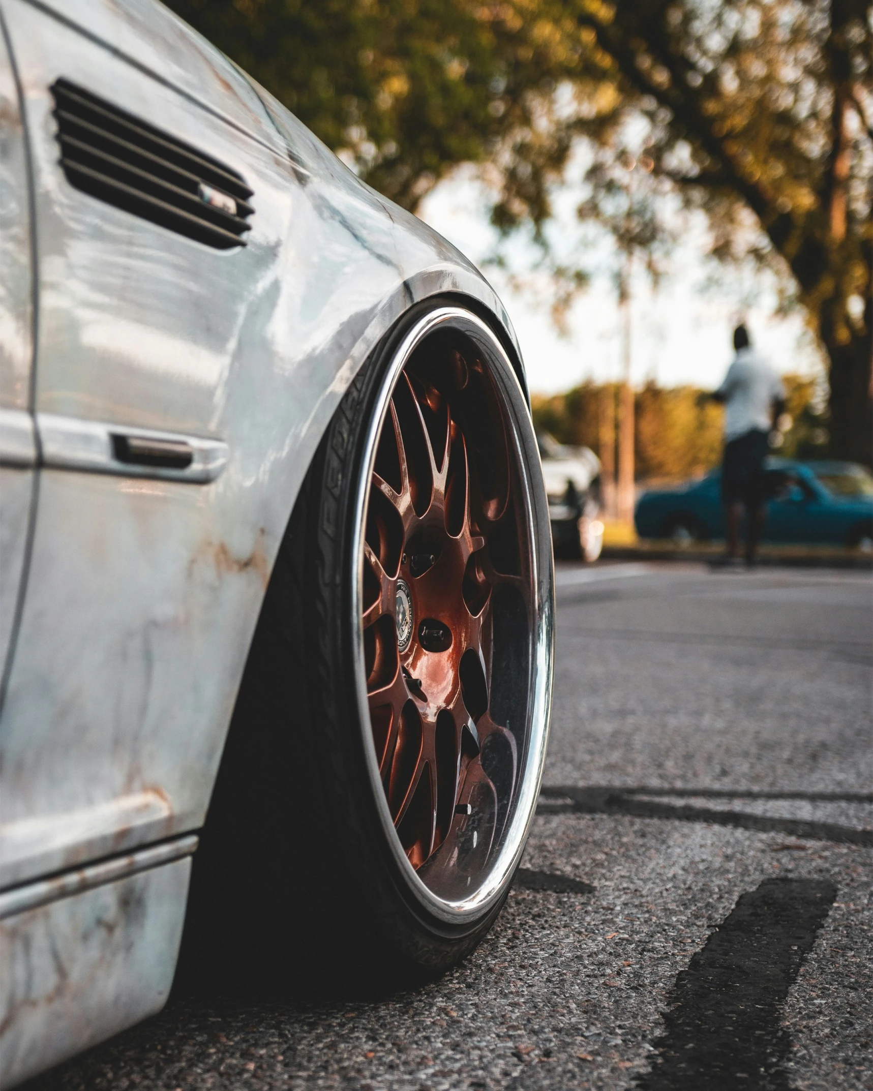 an aluminum car wheel on the pavement and another car parked on the side of the street