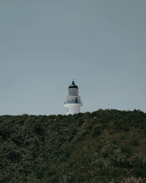 a lighthouse is seen atop of the grassy hill