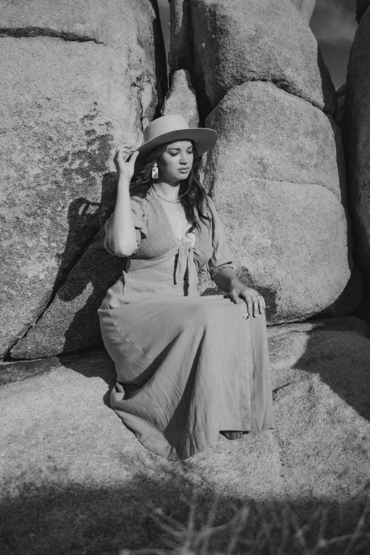 black and white po of woman sitting in front of large rock