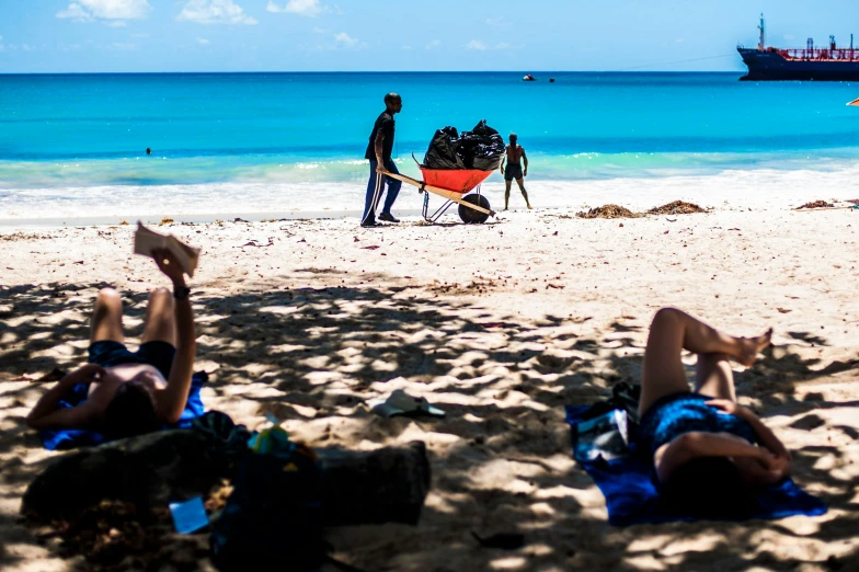 people relaxing on a sandy beach with a cargo ship in the background