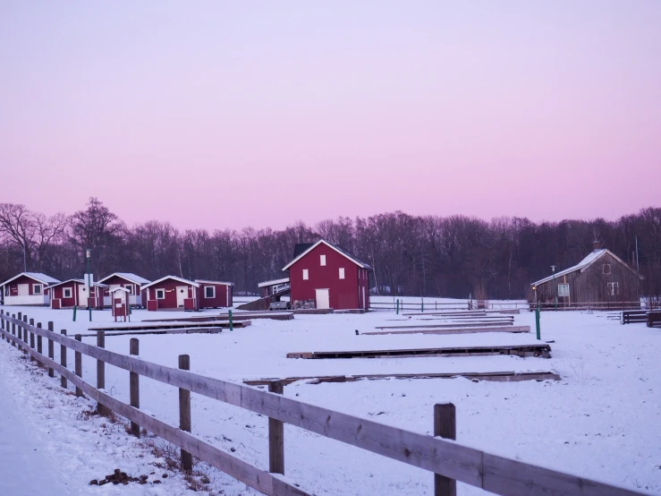 a snowy day in an rural area, with barns, a fence and a fence post