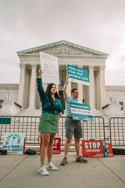 two people holding signs and standing in front of a building