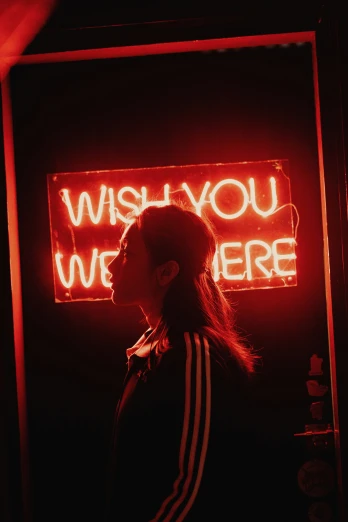 a woman standing in front of a neon sign reading wish you were here