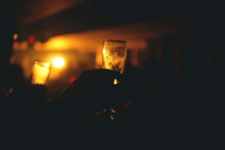 a person holding up a glass with a lit candle in the background