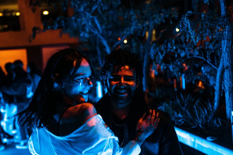 two people are smiling at a party with blue light