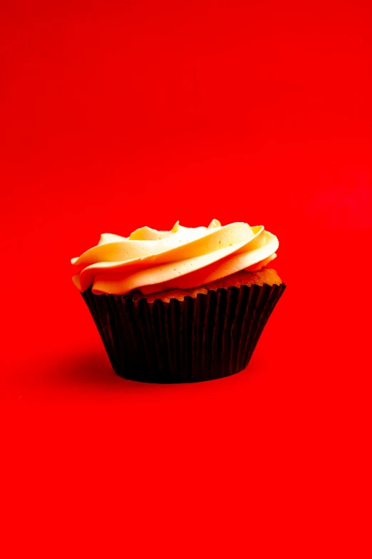 a chocolate cupcake with cream frosting sitting on a red surface