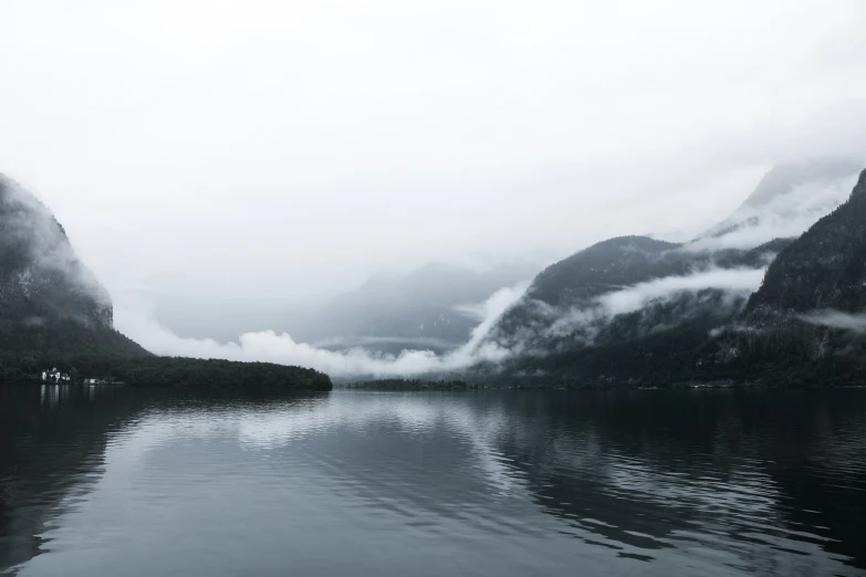 the foggy mountains are reflected in the still waters of the lake