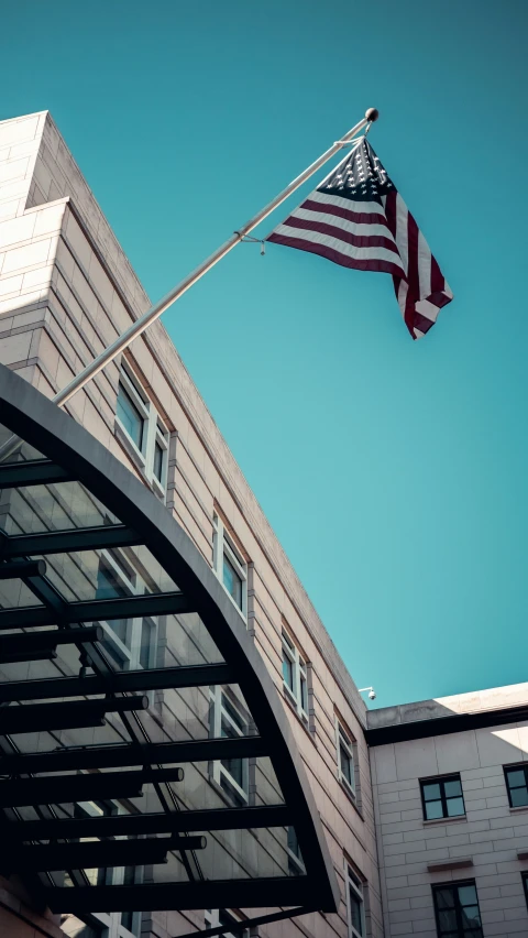 the american flag flying in the wind near the top of a building