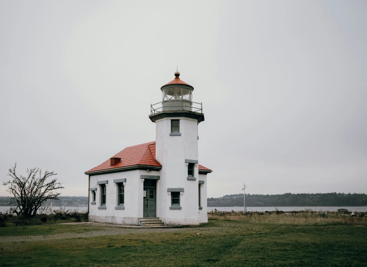 a light house stands in the middle of grass next to a lake