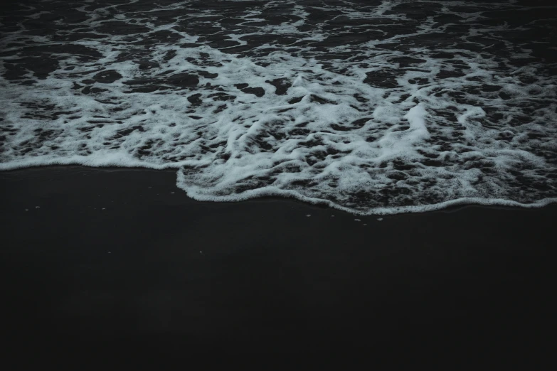 a surfboard is on the black sand of an ocean beach