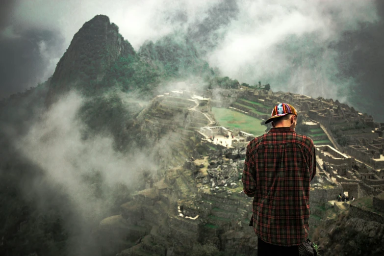 a man with a hat looking at the foggy mountains