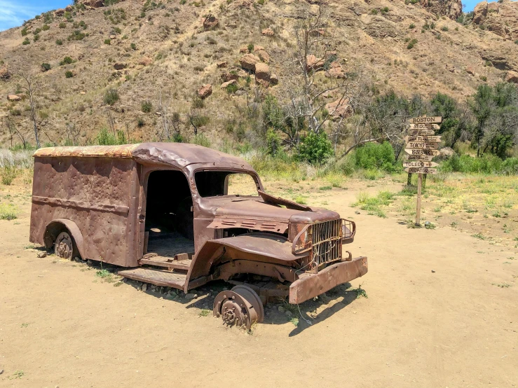 an old rusted out truck parked near a hill