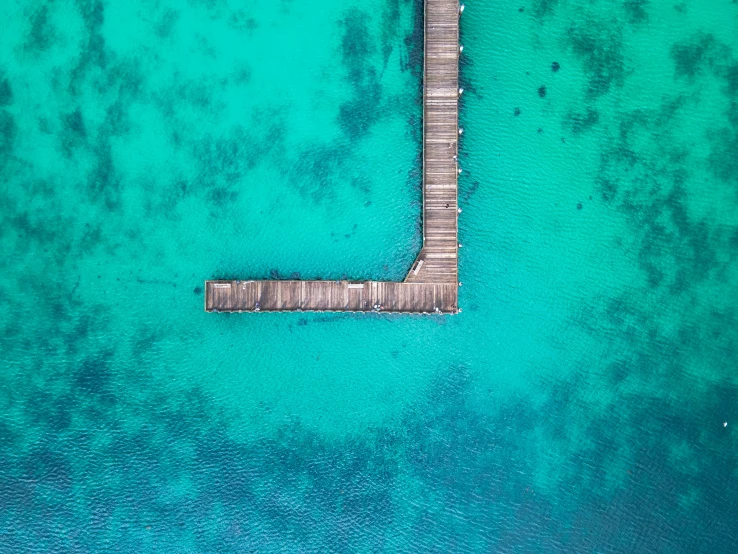 a dock extending to a green ocean with white sand
