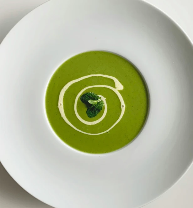 a white bowl filled with green soup and a leafy item