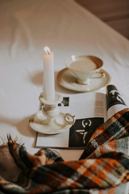 the plaid blanket is next to a candle, plate, and book