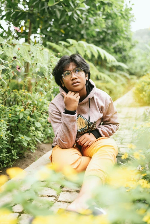 a boy with glasses sitting on the ground in front of yellow flowers