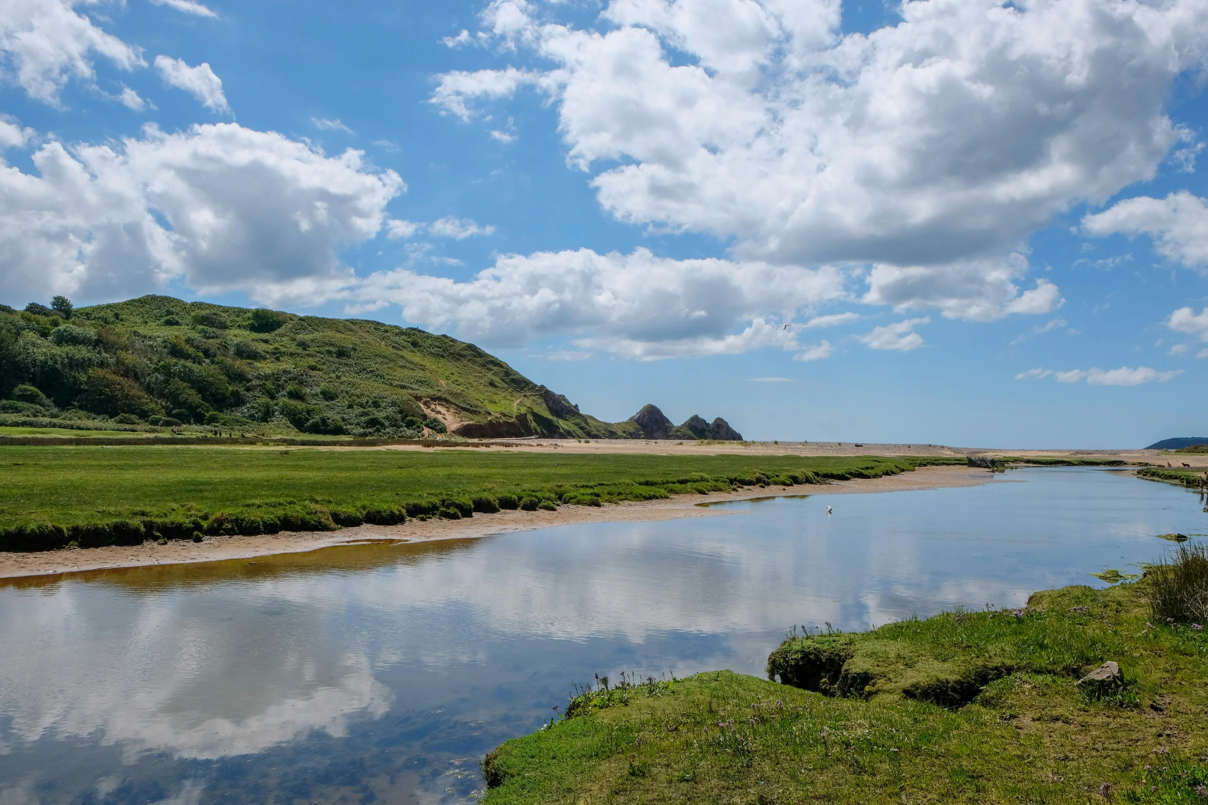 a stream running through the middle of a field next to green hills