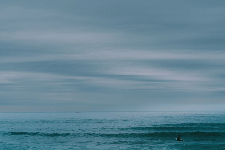 a lone surfer on the ocean with a cloudy sky