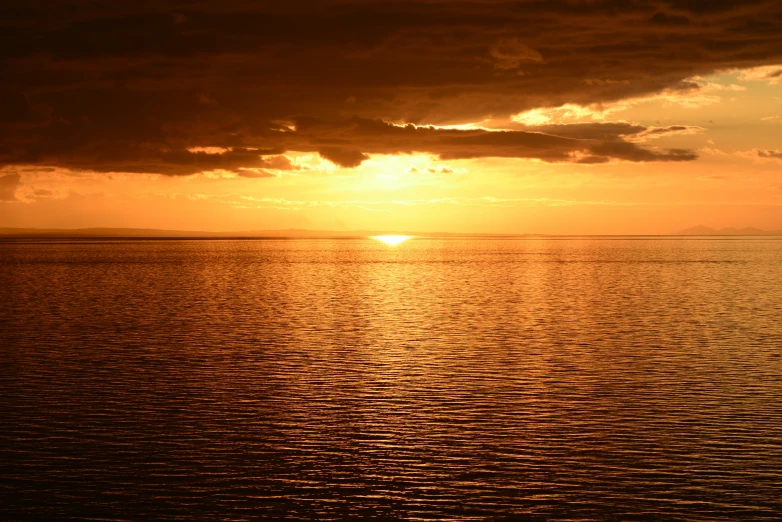 a lone boat sits in the ocean as the sun sets