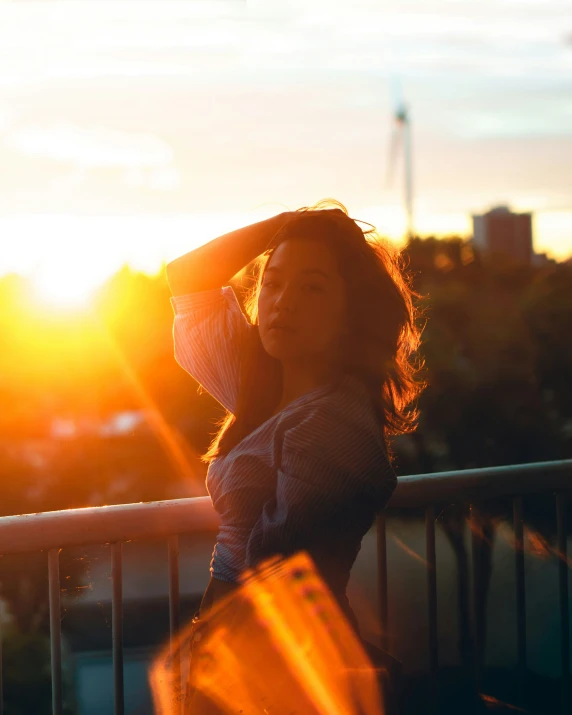 a woman is standing near a fence at sunset