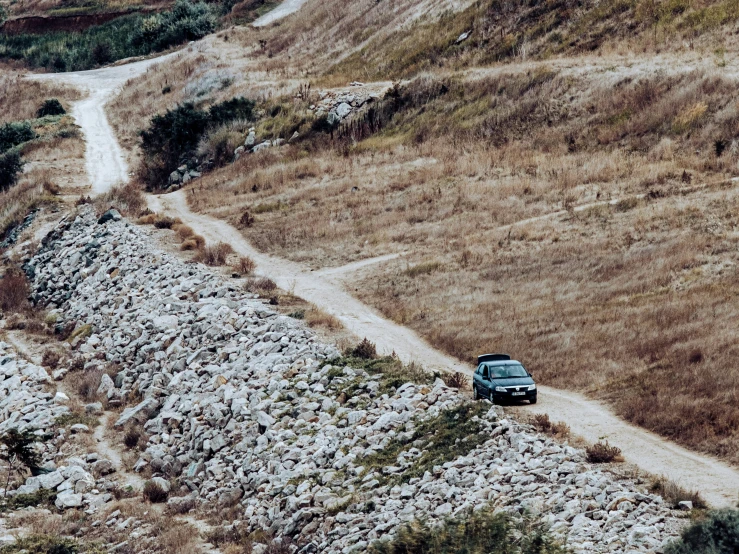 vehicle driving on dirt road near rocky and grassy hill