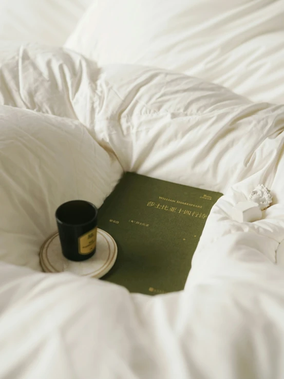 an opened book, a cup and a black coffee sitting on a bed