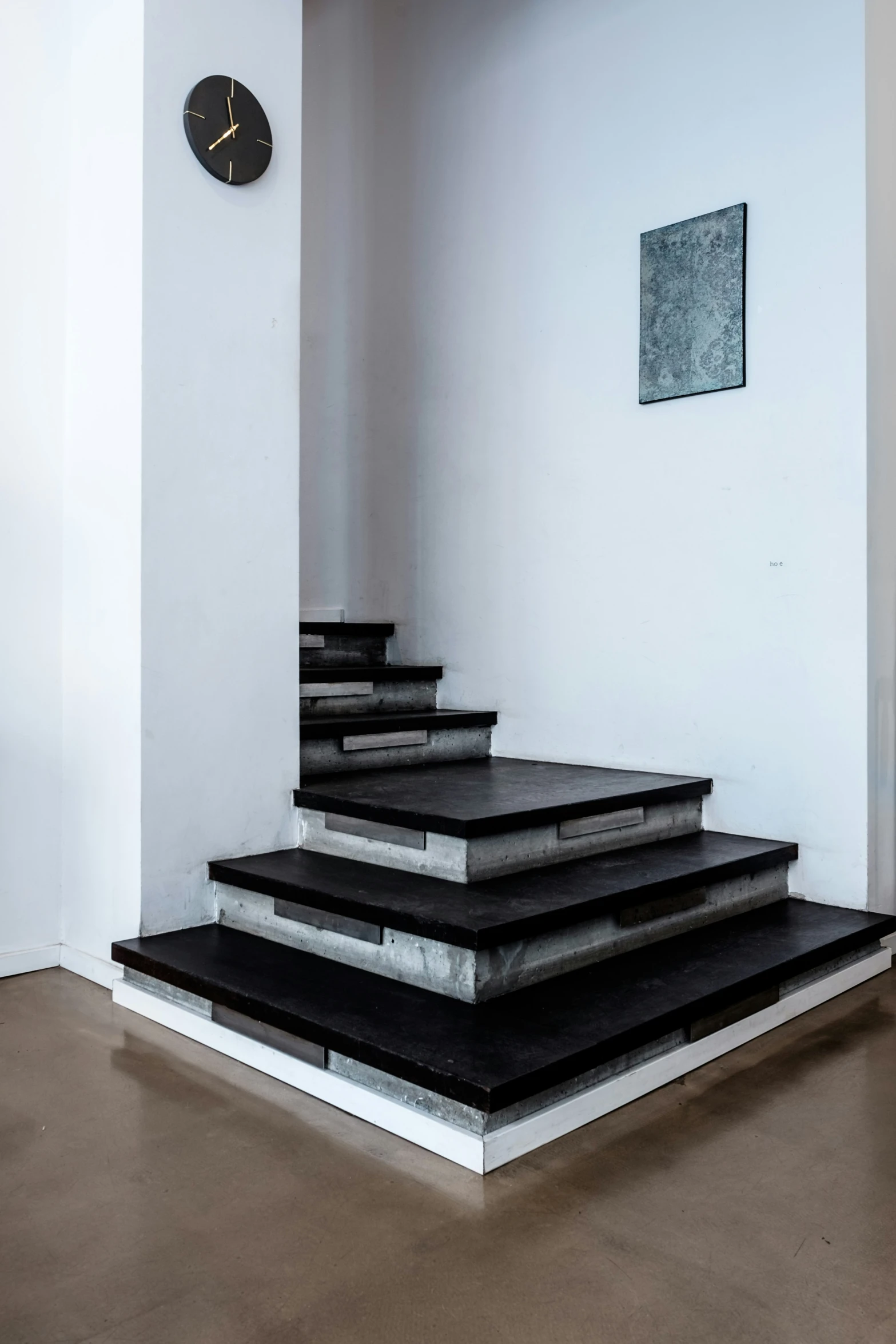 an empty white room with concrete steps leading to a clock