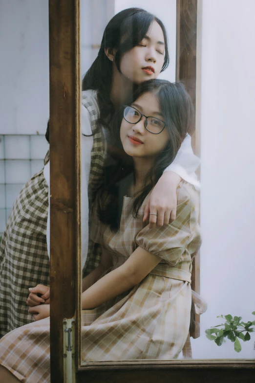 two women sitting down behind a mirror and one is hugging