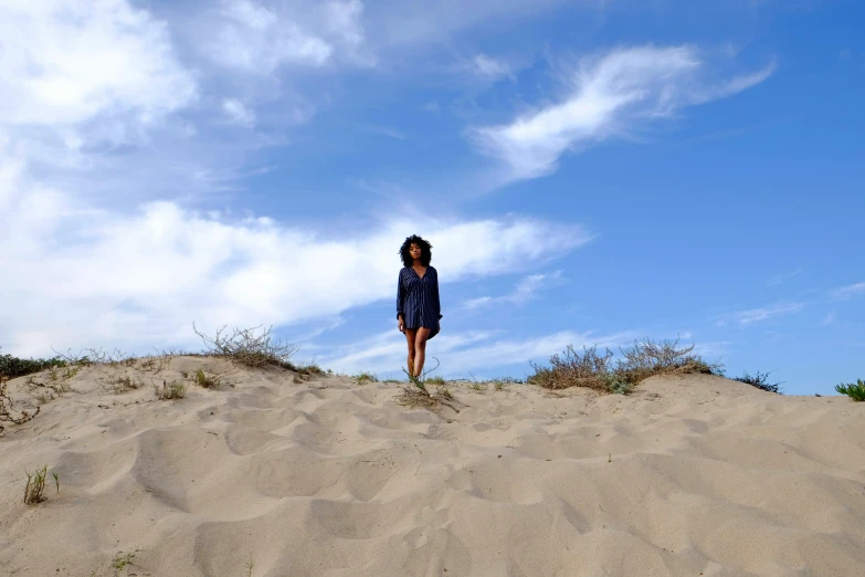 a girl in a dress standing on a beach dune