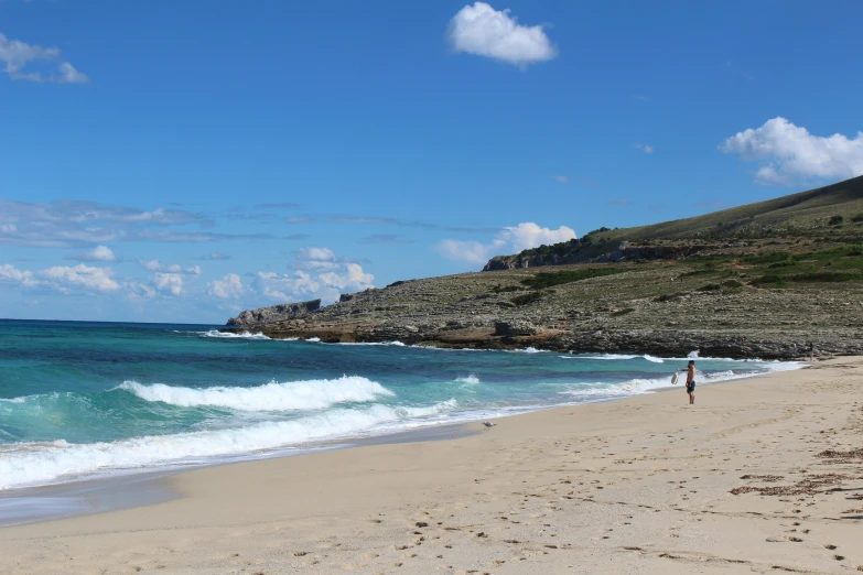 two people are walking along the beach near the water