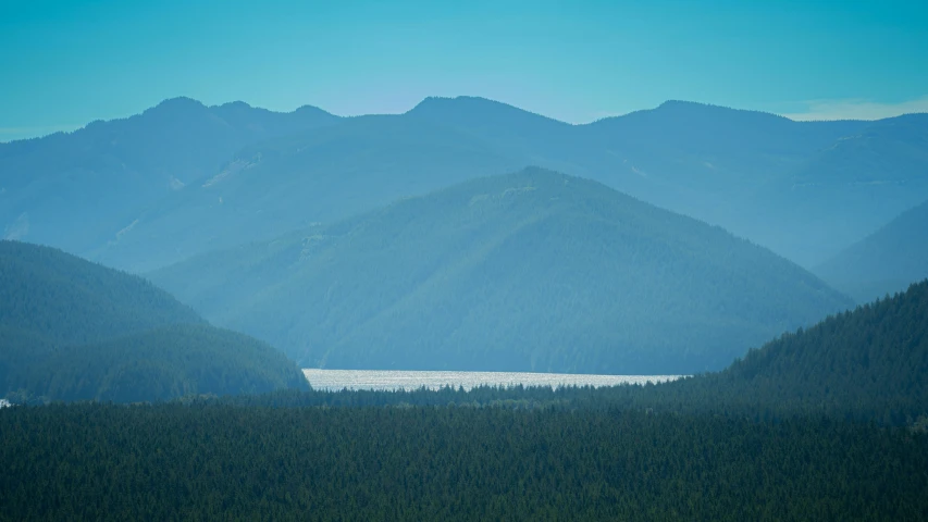 a mountain range in the foreground with a body of water surrounded by woods