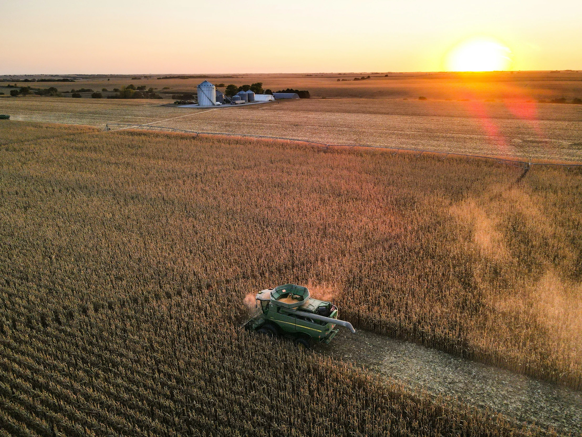 a combine harvester in a field with a setting sun