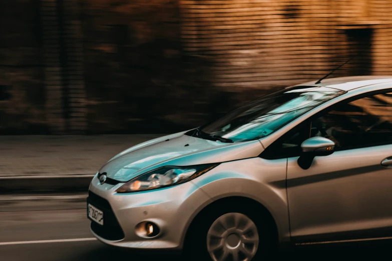 a blue car driving on a road next to a brick wall