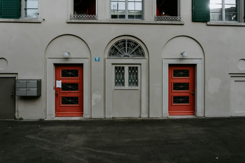 two red doors and windows with green shutters in front of a white building