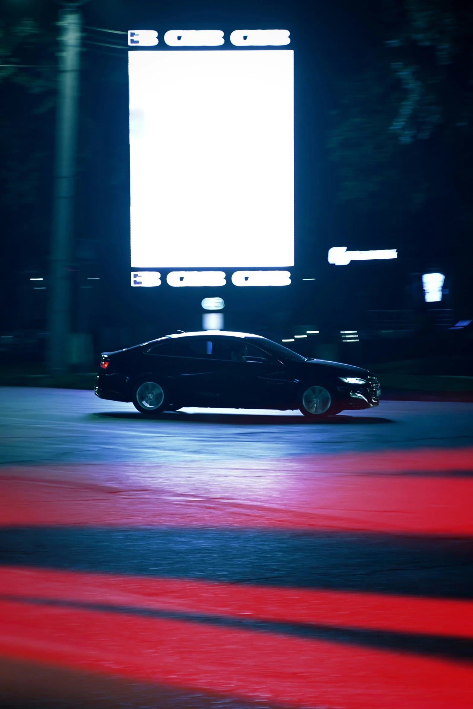 a black car stopped in a parking lot with a large screen behind it