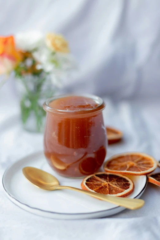 a jar of liquid with golden spoons sits on a plate