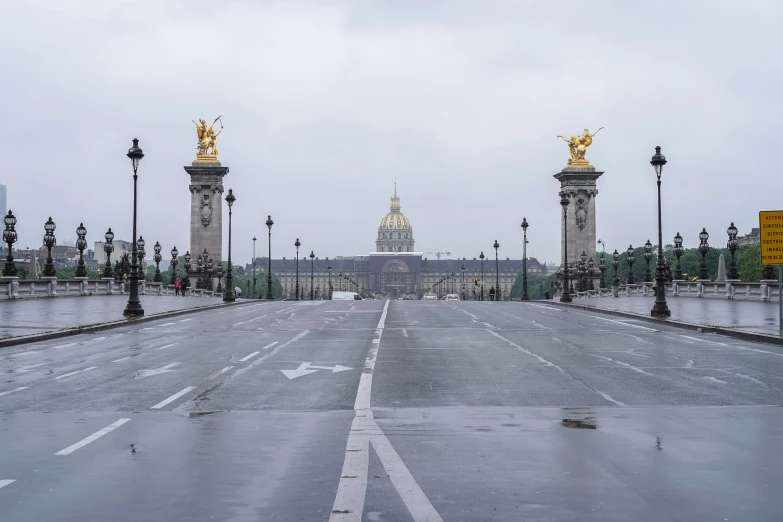 wet pavement and lampposts in an open road with building in background