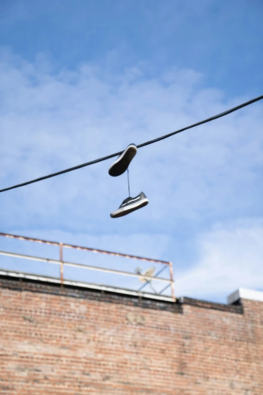 pair of tennis shoes hanging from wire with brick wall and blue sky background