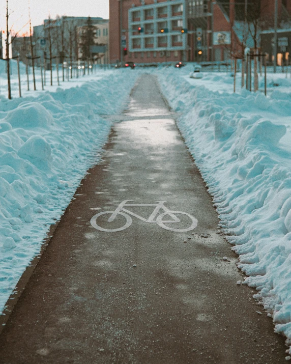 a path is lined with mounds of snow, and the bicycle trail has been marked on