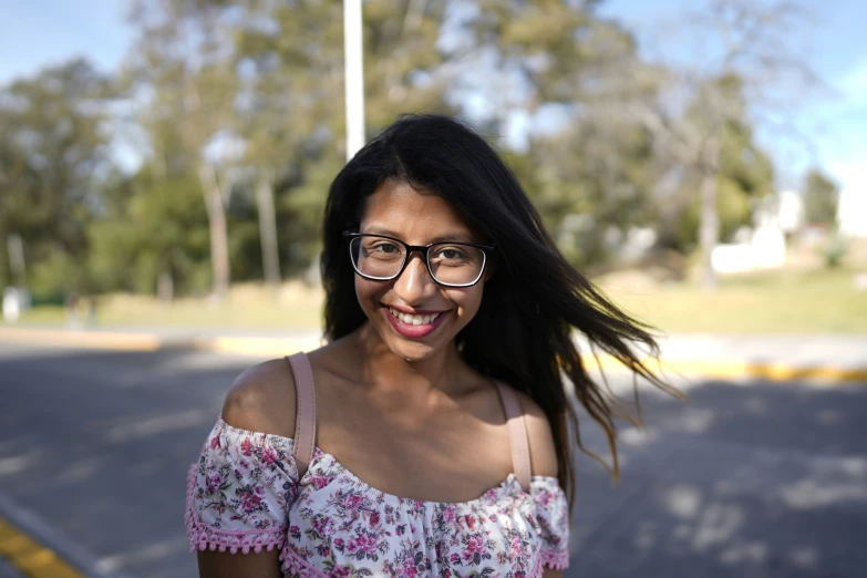 a woman with long hair and glasses smiling in the street