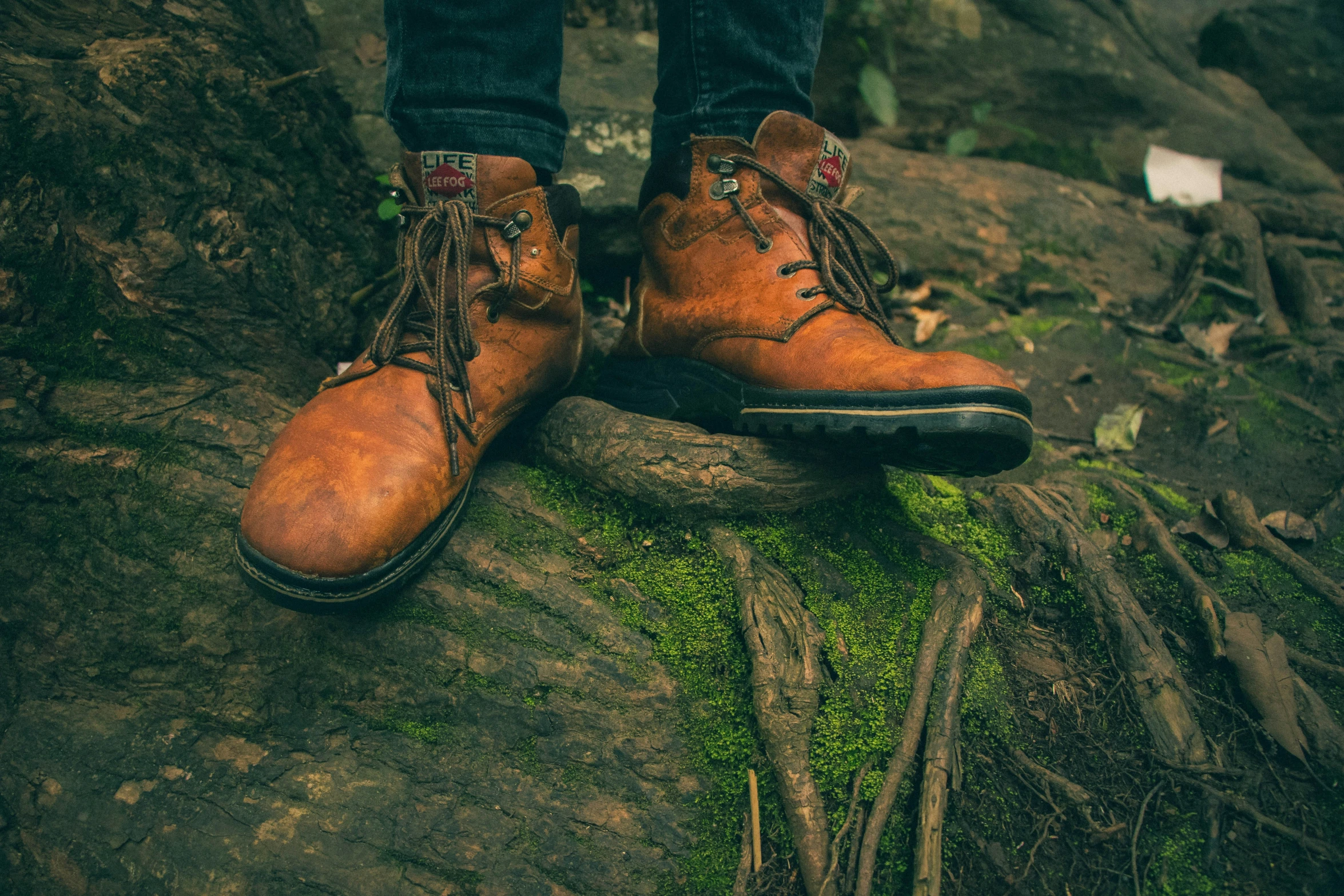 two legs in boots standing on top of mossy rock