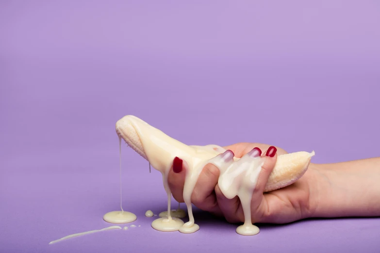 two hands holding banana slices with icing on a purple background