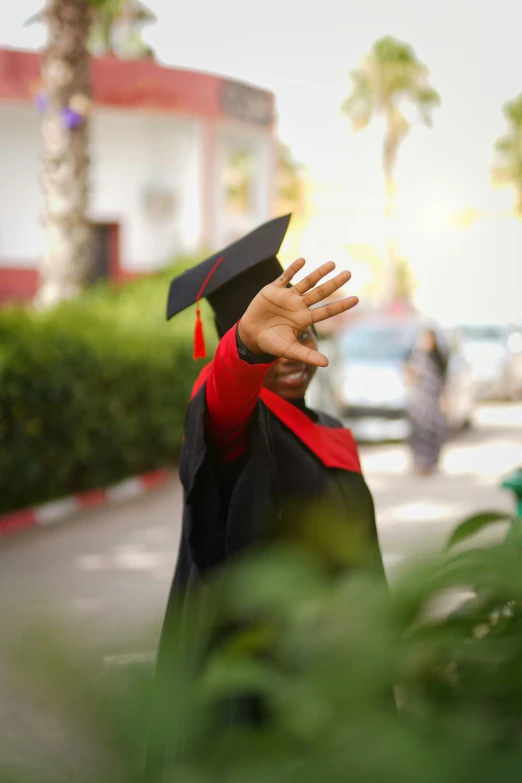 a man holding his hand up while wearing a black graduation hat