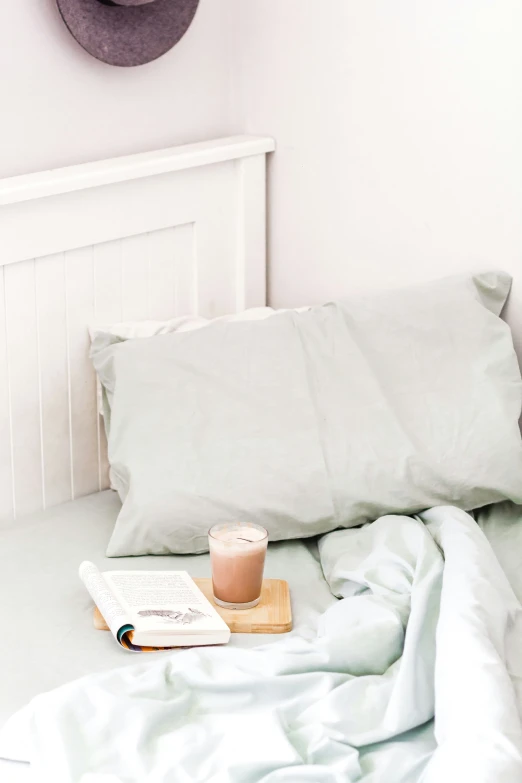 a bed with two pillows and a cup of drink on top