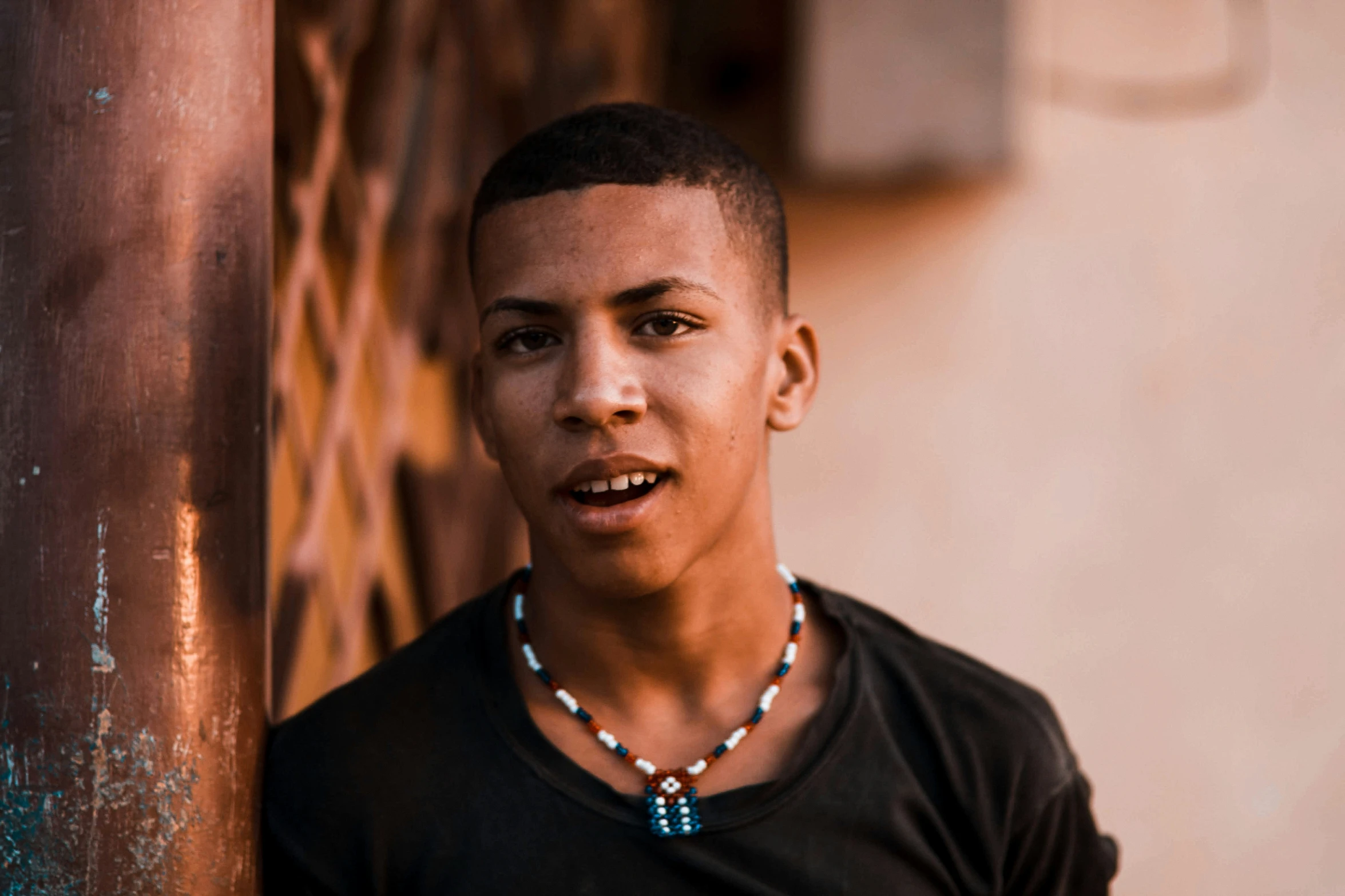 young man wearing beaded necklace and standing by pole