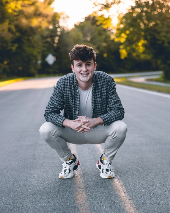 a young man crouches down to pose for a po on an empty street