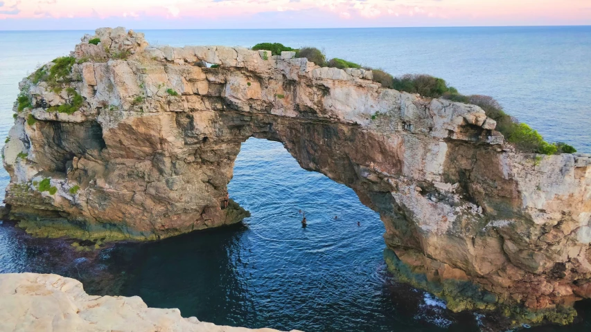 an island in the middle of some water, with a rock arch